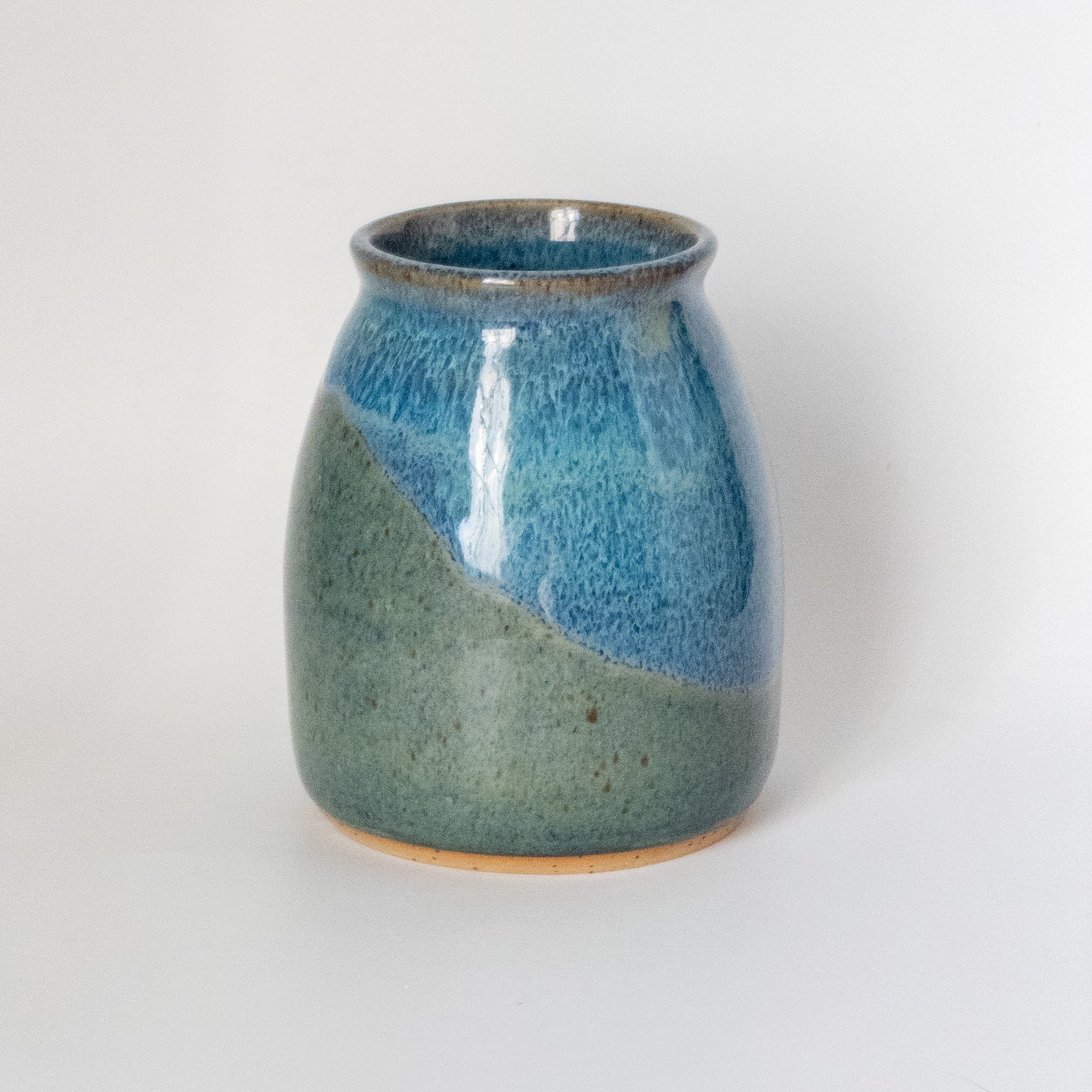 Wheel thrown ceramic vase with blue and green glaze inspired by a mountain landscape on a white background