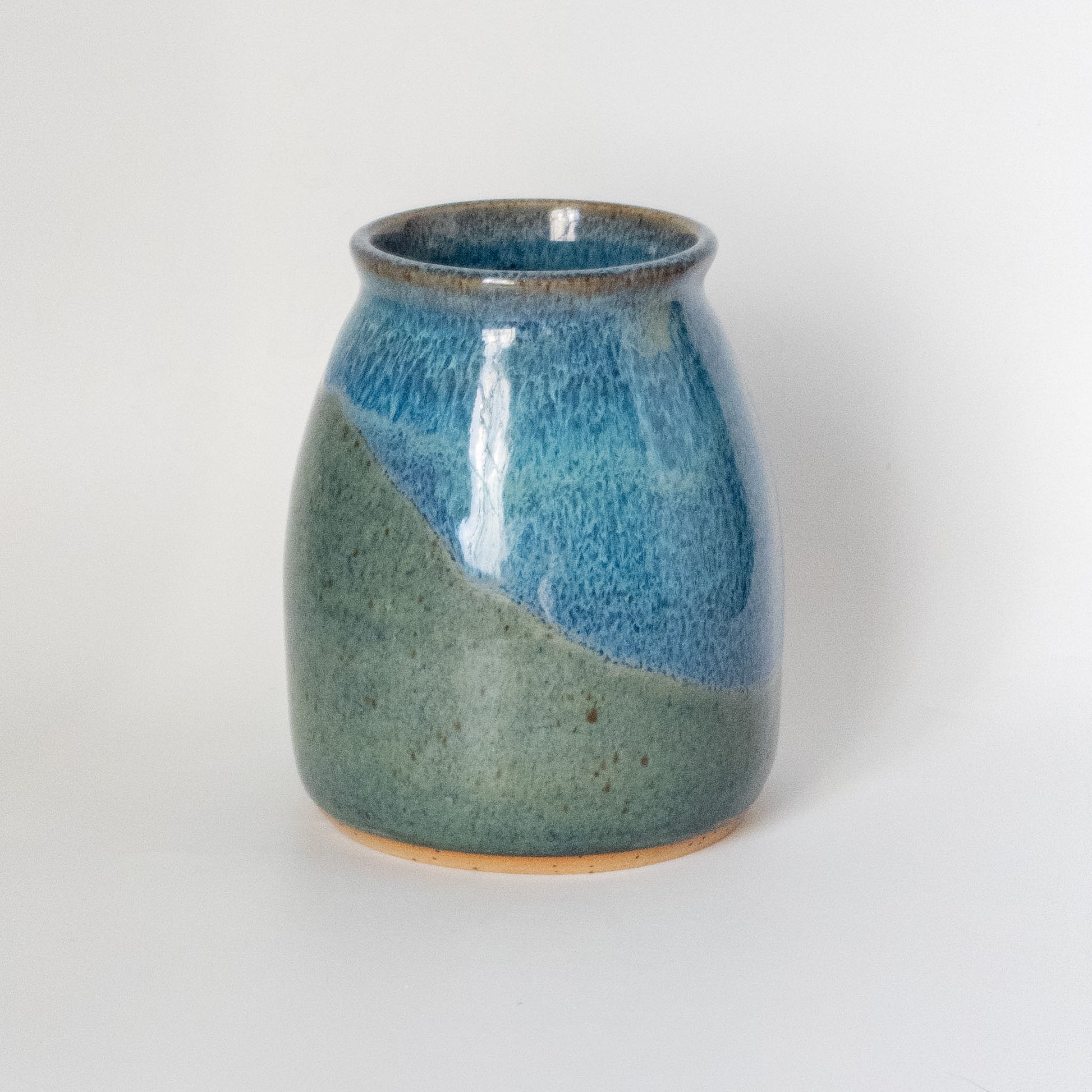 Wheel thrown ceramic vase with blue and green glaze inspired by a mountain landscape on a white background
